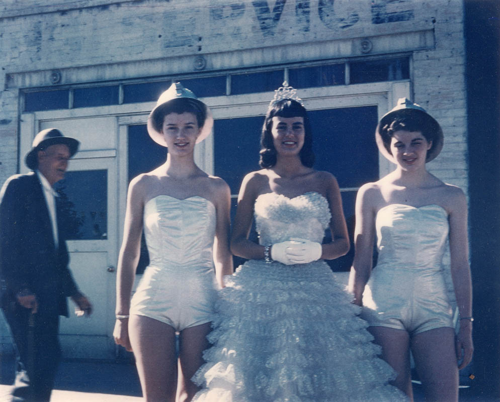 An unidentified man appears to be enjoying the sun and the fun along with Wallace Silver Jubilee participants waiting to board their float for the Spokane Lilac Festival parade in 1958. Princesses Camille Betts and Barbara Britt in mining hats flank Queen Cleo Bardelli (Clizer).