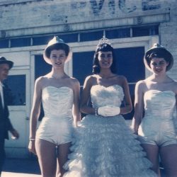An unidentified man appears to be enjoying the sun and the fun along with Wallace Silver Jubilee participants waiting to board their float for the Spokane Lilac Festival parade in 1958. Princesses Camille Betts and Barbara Britt in mining hats flank Queen Cleo Bardelli (Clizer).